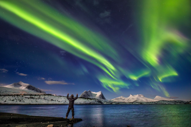 Mann som står med hendene opp i flott natur under Nordlyset